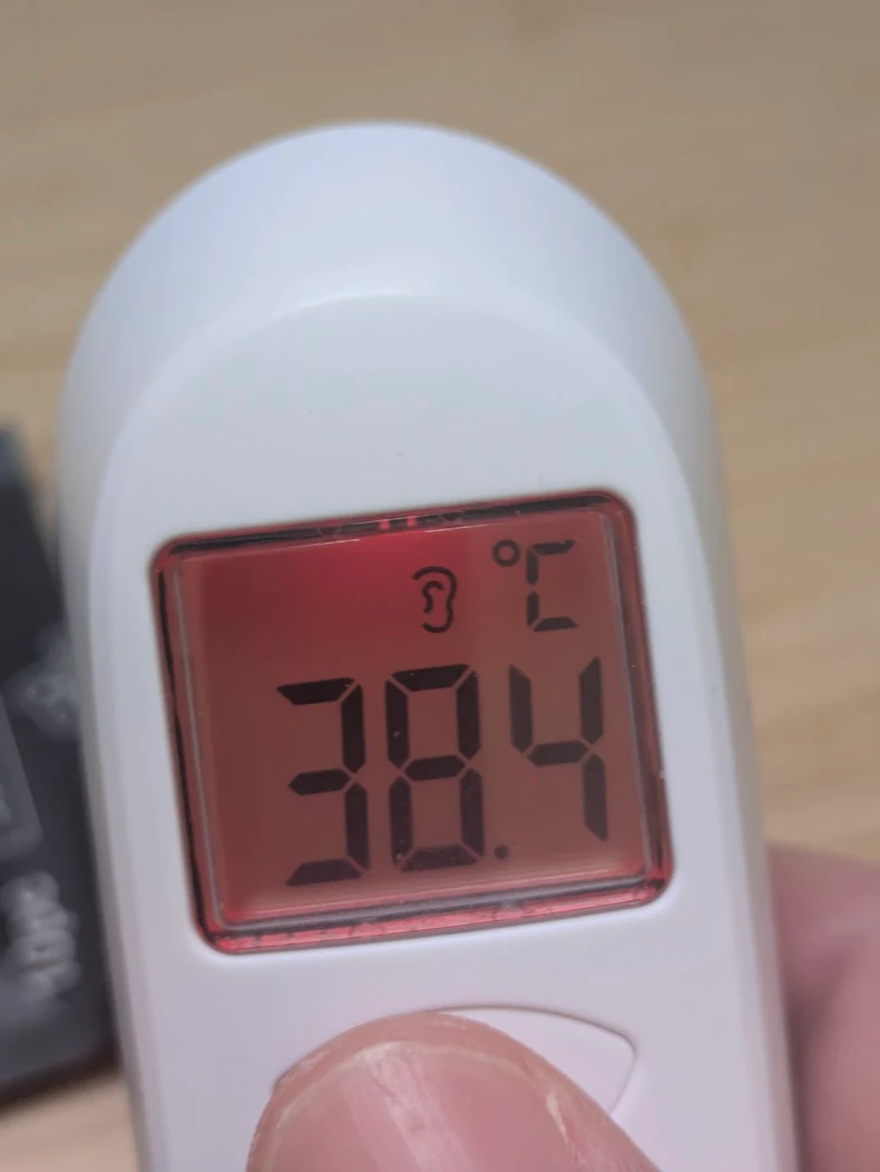 a white infrared ear thermometer that displays 38.4C with a red background