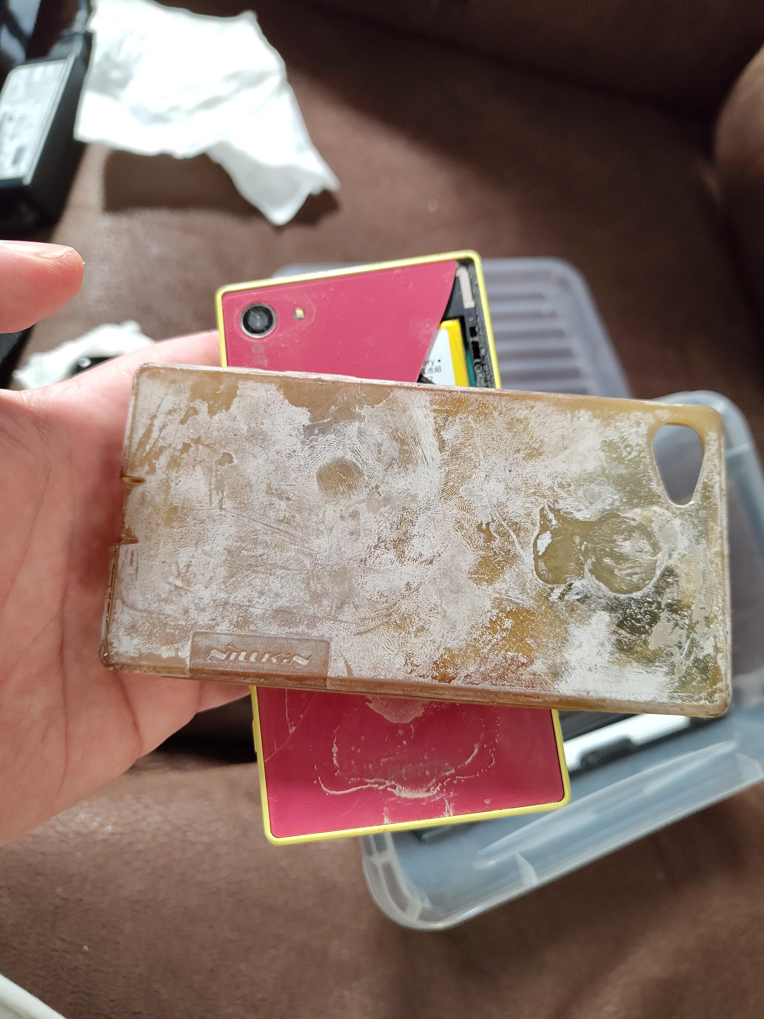 the moldy case removed, laying on the red cracked back of the phone's backside (it's a yellow phone but I replaced the battery once when I still used it)