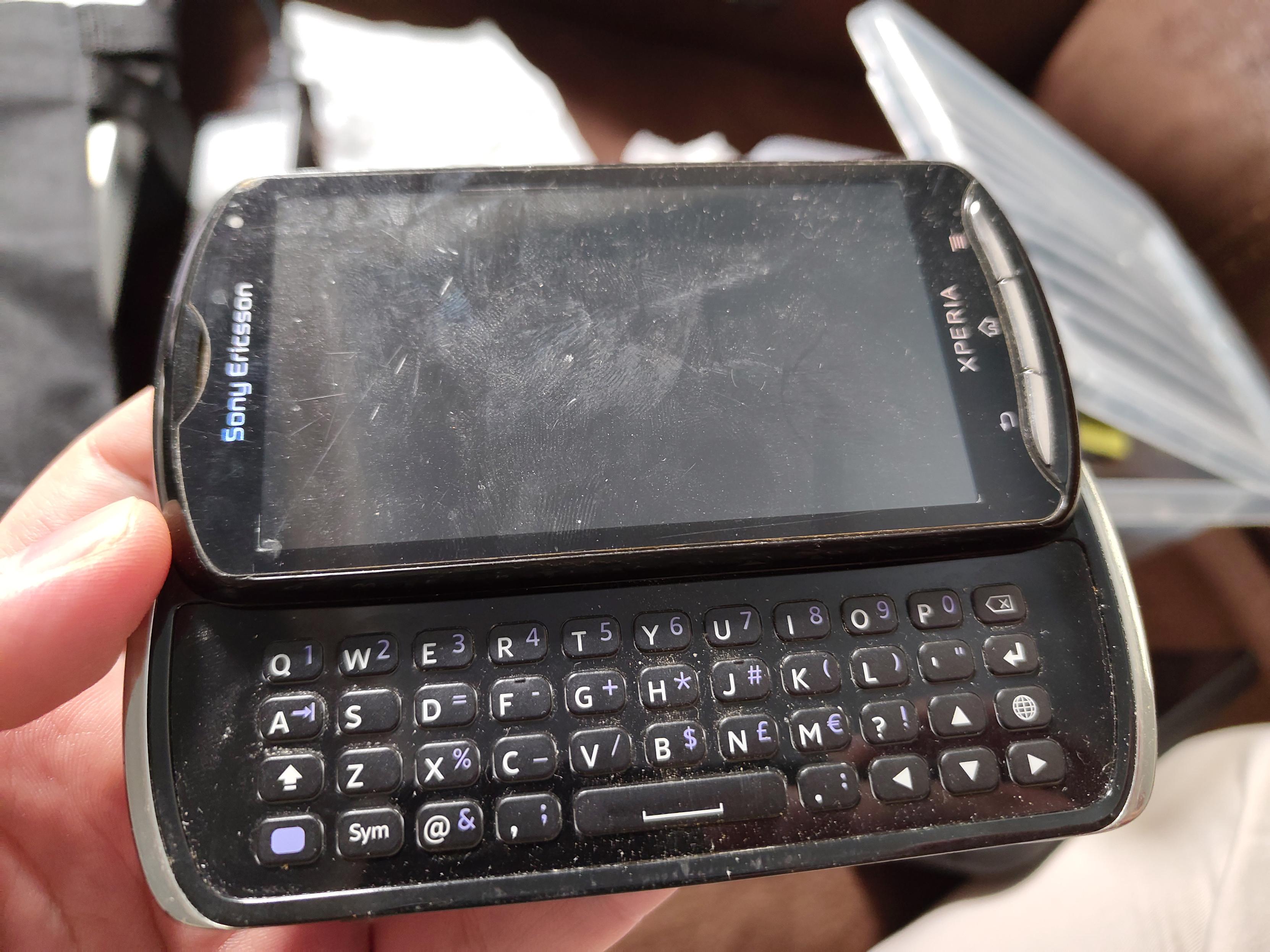 A black Sony-Ericsson Xperia Pro Mk16i. It is slid open, revealing the fullsize keyboard underneath the screen. It was a rather small device that fit in your hand just like the Nokia