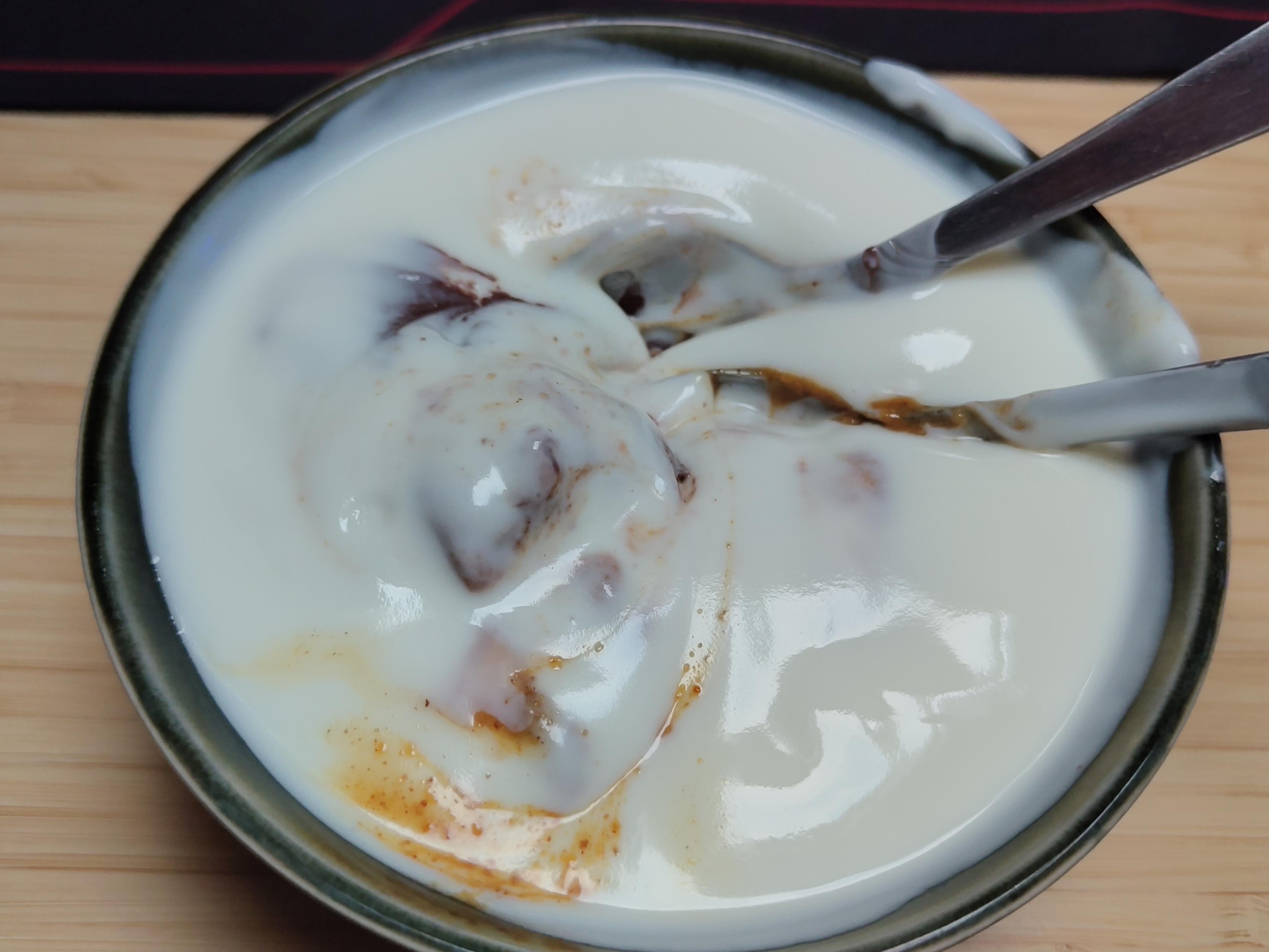 a small bowl with two spoons, filled to the brim with white yogurt, some chunky colors of chocolate and peanut butter browns mixed into the substance