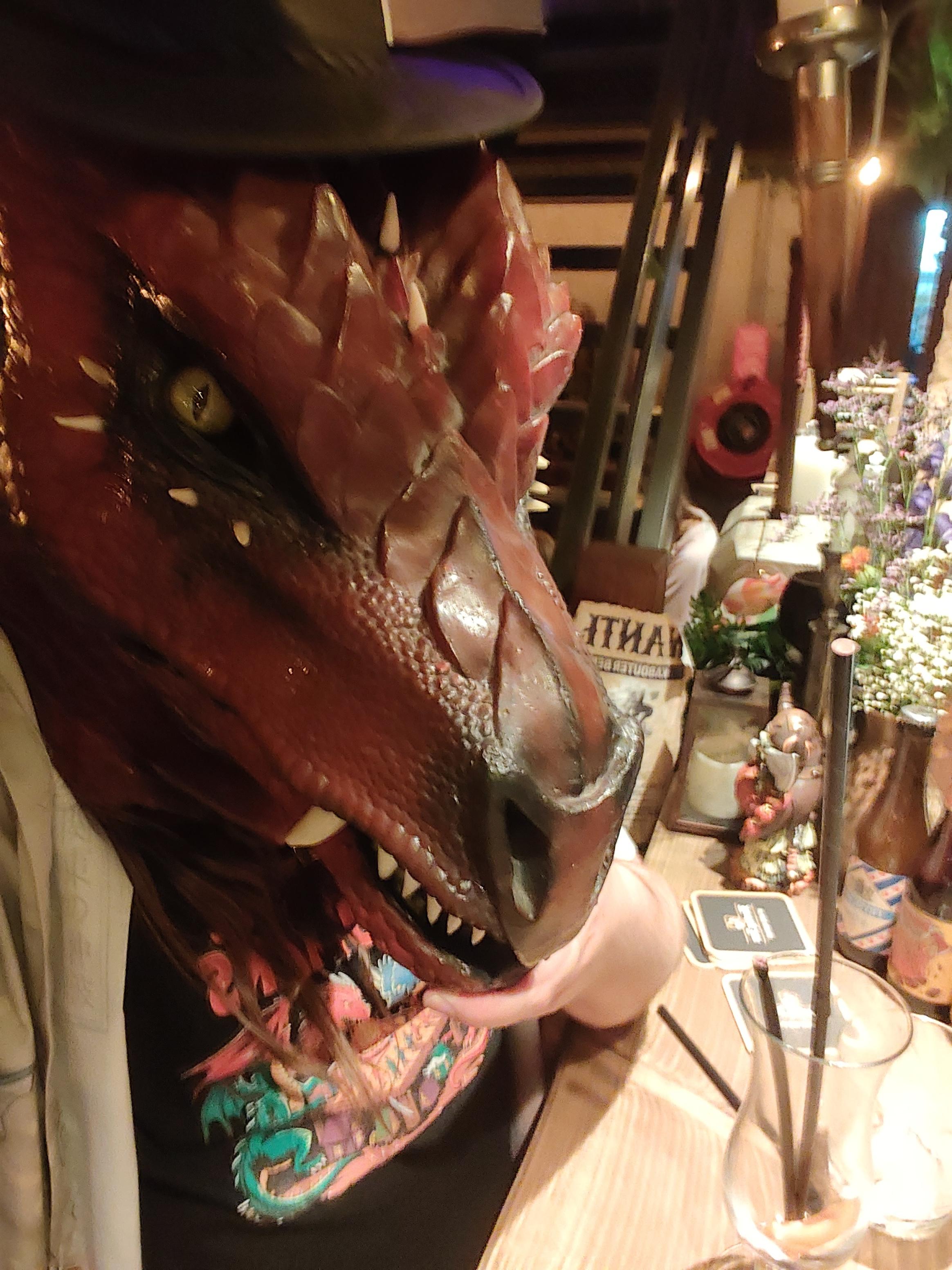 a realistic red dragon head fursuiter (still with the big leather hat on) sitting at a bar with an empty glass of something (was it mead? it might've been mead. 7 glasses of mead? maybe, who are you to confirm or deny? are you gonna challenge the dragon? who might've drank too much? careful you might get burned. or drunk. or both)